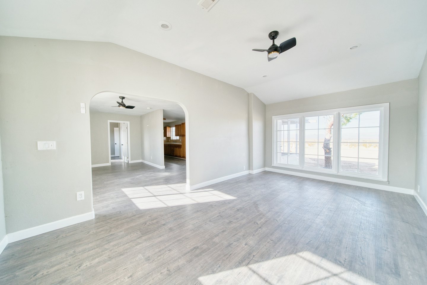 Empty living room with light grey walls and wood flooring.