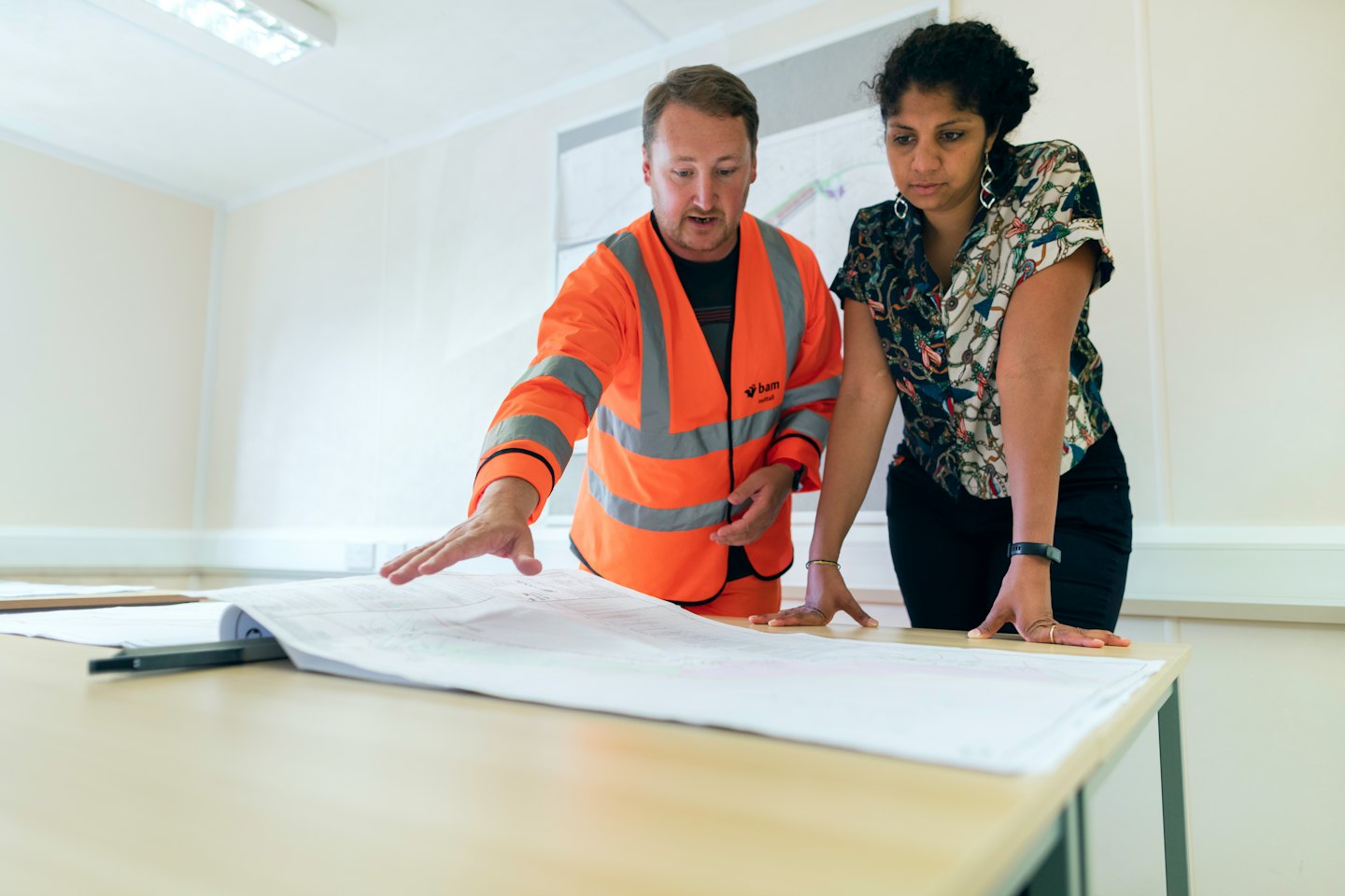 Two professionals review blueprints on a wooden table.