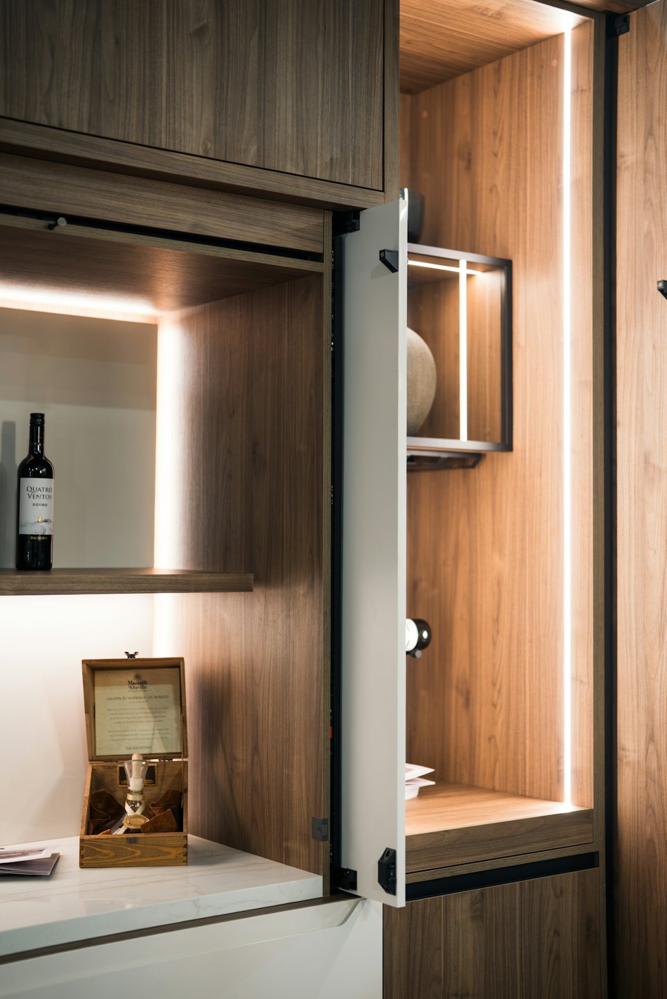 Modern wooden cabinetry features illuminated shelves and a marble countertop.