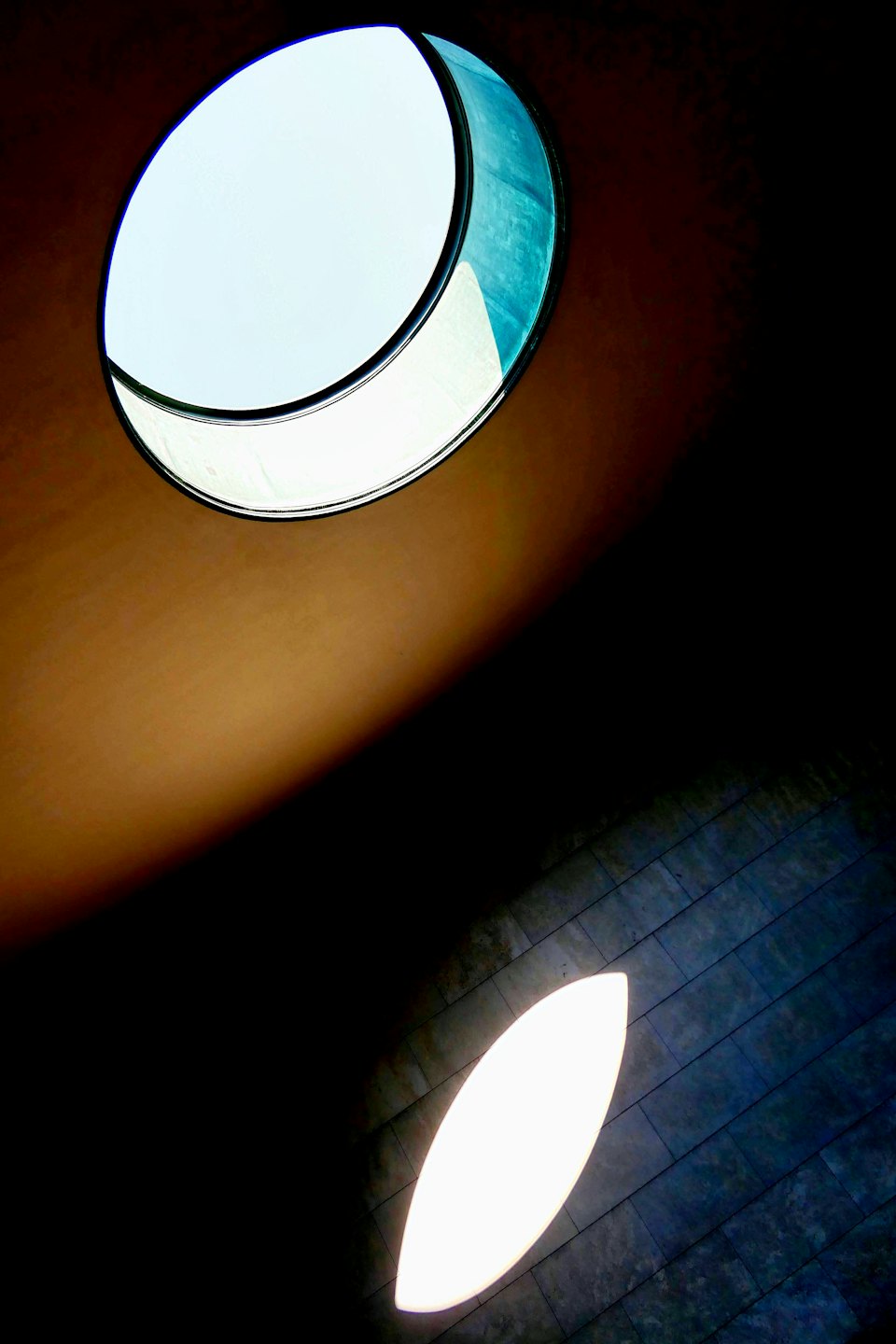 A circular skylight reflects onto a dark tiled floor.